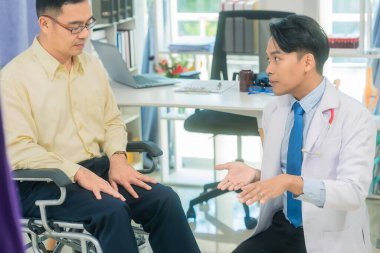 Genç bir Asyalı doktor tekerlekli sandalyedeki yaşlı bir hastayla konuşuyor, sağlık, tıp veya hastane işleriyle ilgili fikirleri tartışıyor..
