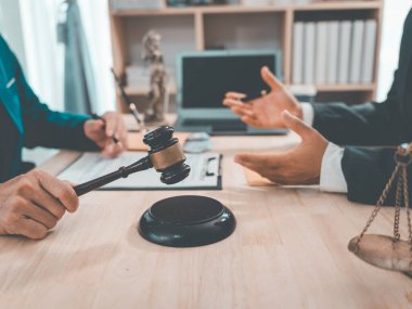 Avukat, arkaplanda hukuki süreci sembolize eden bir tokmak ve mahkeme salonunda bir dizüstü bilgisayarla çalışıyor..