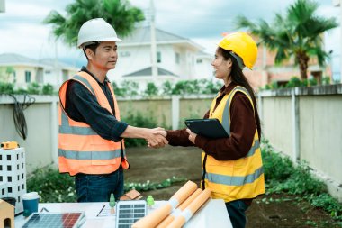 Mühendisler ve mimarlar inşaat alanında el sıkışıyor ve projeyi tartışıyorlar. Mühendisler ve ekipleri, planlarla el ele tutuşarak inşaat alanının geliştirilmesi konusunda anlaştılar..