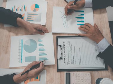 A team of business professionals is discussing charts and graphs on a tablet regarding business investments and growth, illustrating the results of teamwork. (Close-up view)