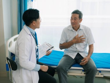 Asyalı bir erkek doktor ve yaşlı bir hasta hastane odasında bir yatakta konuşuyorlar..