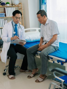 Asyalı bir erkek doktor ve yaşlı bir hasta hastane odasında bir yatakta konuşuyorlar..