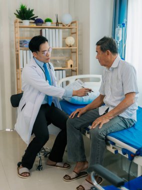 Asyalı bir erkek doktor ve yaşlı bir hasta hastane odasında bir yatakta konuşuyorlar..