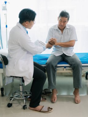Asyalı bir erkek doktor ve yaşlı bir hasta, hastane koğuşunda hastaya yardım etmek için fizyoterapi yapmak üzere el ele tutuşur..