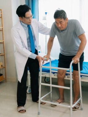 Yaşlı bir erkek hasta, Asyalı bir erkek doktorun gözetiminde, yaşlılar koğuşuna girmek için baston kullanıyor..