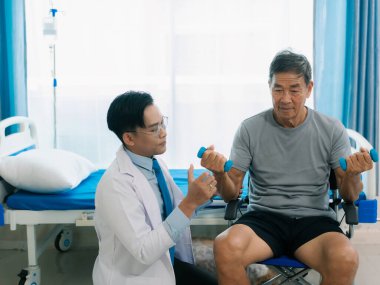 Asyalı bir erkek doktor, terapi ve dayanıklılık eğitimi için yaşlı bir adama tekerlekli sandalyedeki bir adama halterli rehabilitasyon egzersizleri önerdi..