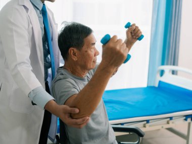 Asyalı bir erkek doktor, terapi ve dayanıklılık eğitimi için yaşlı bir adama tekerlekli sandalyedeki bir adama halterli rehabilitasyon egzersizleri önerdi..
