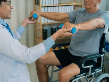 Asyalı bir erkek doktor, terapi ve dayanıklılık eğitimi için yaşlı bir adama tekerlekli sandalyedeki bir adama halterli rehabilitasyon egzersizleri önerdi..