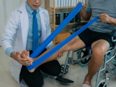 Yaşlı bir Asyalı, yatakta yatarken bacaklarını ve dizlerini esnetebilmek için fizyoterapi görüyor..