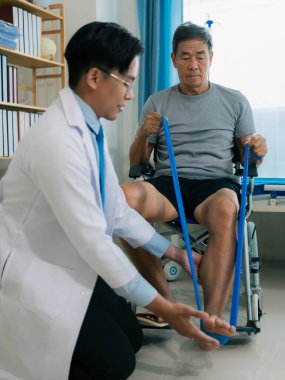 Yaşlı bir Asyalı, yatakta yatarken bacaklarını ve dizlerini esnetebilmek için fizyoterapi görüyor..