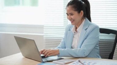 Asyalı bir iş kadını masasındaki mali raporları analiz ediyor. Harcamaları, grafikleri ve dizüstü bilgisayarını kullanarak gelir ve giderleri hesaplıyor..