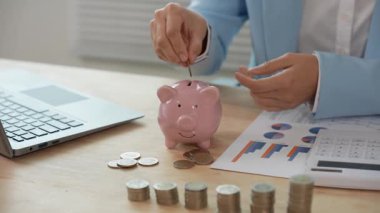 Asyalı bir iş kadını masasındaki mali raporları analiz ediyor. Harcamaları, grafikleri ve dizüstü bilgisayarını kullanarak gelir ve giderleri hesaplıyor..