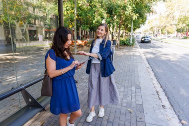 Bir otobüs durağında elinde kağıt haritayla güzergahlarını tartışan gülümseyen kadınlar.
