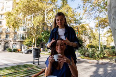 Kafe terasında konuşan ve gülen iki kadının doğal anı, şehirde bağlantı ve neşe gösteriyor..