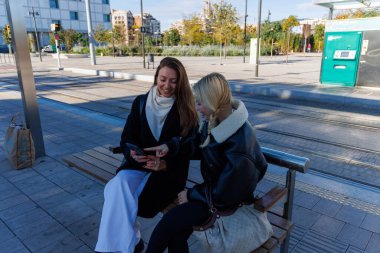 İki arkadaş tramvay istasyonunda oturup, sakin bir şehirde, dinlenip, konuşarak ulaşımı bekliyorlar.
