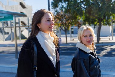 İki arkadaş tramvay istasyonunda oturmuş tramvaylarını beklerken rahat bir sohbetin tadını çıkarıyorlar.