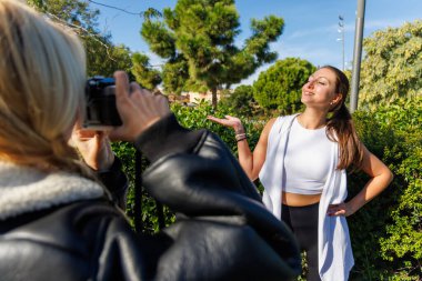 İki arkadaş poz vermek ve klasik bir kamerayla fotoğraf çekmek için durur. Parkta huzurlu ve aydınlık bir yürüyüşün tadını çıkarırlar..