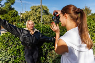 İki arkadaş, parkta yürürken klasik bir kamera kullanarak doğal ve sakin bir ortamın keyfini çıkarırken birbirlerini yakalıyorlar..