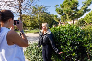 İki kadın parkta yürürken eski tarz fotoğraflar çekiyorlar. Dostça ve rahat bir atmosferi paylaşıyorlar..