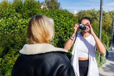 İki arkadaş güneşli bir parkta yürürken eski bir kamera için poz veriyor, sıcak ve neşeli anılar yaratıyorlar..
