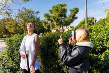 İki kadın, parkta sakince yürürken eski tarz fotoğraflar çekmek için eski bir kamera kullanıyor..