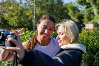 İki kadın, yeşil ve sessiz bir parkta sakince dolaşırken klasik bir kamerayla nostaljik selfie çekiyorlar..