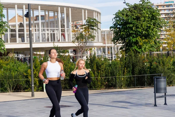 Spor kıyafetleriyle koşan iki kadın parkta sabit bir tempoda koşuyor..