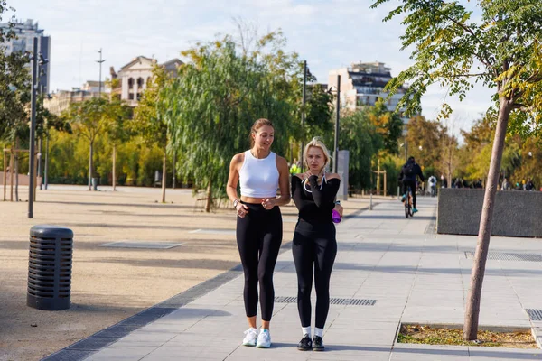 Parkta spor kıyafetleri içinde koşan iki kadın aktif bir yaşam tarzını paylaşıyor..