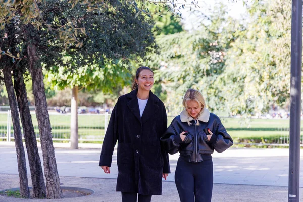 İki arkadaş parkta sakince sohbet ediyor, anlarını paylaşıyor ve doğal ve açık bir ortamda huzurlu bir yürüyüşün tadını çıkarıyor.