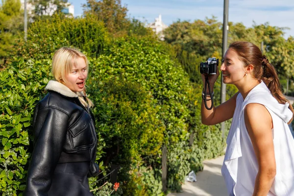 İki arkadaş gülüyor ve klasik bir kamerayla eski tarz fotoğraflar çekiyor. Parlak ve hoş bir parkta yürürken..