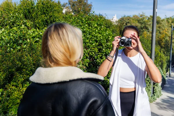 İki arkadaş güneşli bir parkta yürürken eski bir kamera için poz veriyor, sıcak ve neşeli anılar yaratıyorlar..