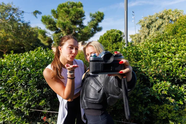 İki arkadaş, sakin ve doğal bir parkta yürürken eski bir kamerayla eski tarz selfie çekiyorlar ve poz veriyorlar..