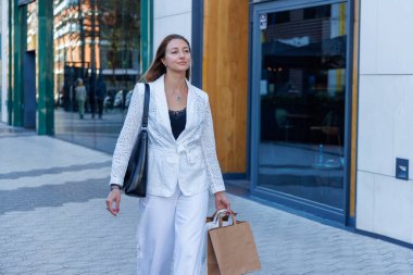 Mağazalar, alışveriş torbaları arasında rahatça yürüyor. Satış promosyonları ve modern mağaza dekorasyonu onu büyülüyor.