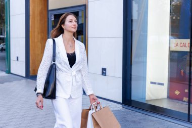 Mağazalar, alışveriş torbaları arasında rahatça yürüyor. Satış promosyonları ve modern mağaza dekorasyonu onu büyülüyor.