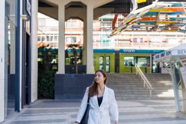 Alışveriş yapan biri, moda ürünleri seçmeyi bekleyen çantalarla dolu satış afişleri altında vitrin mankenlerini incelemek için durur.