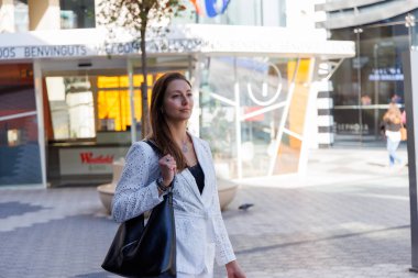 Şık bir kadın şık mağaza vitrinlerinin önünde durur, elinde çantalar, canlı satış etiketleri, alışveriş çılgınlığı sırasında dikkatini çeker.