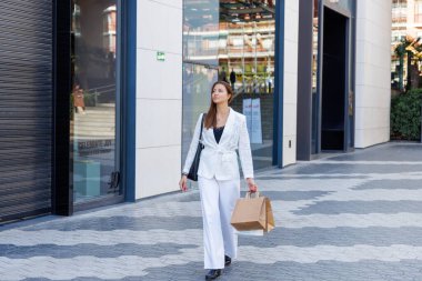 Mağazalar, alışveriş torbaları arasında rahatça yürüyor. Satış promosyonları ve modern mağaza dekorasyonu onu büyülüyor.