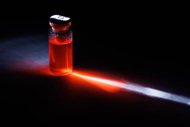 Keskin bir ışık demeti altındaki mermer yüzeyine yansıyan renkli sıvıyla dolu canlı cam tıbbi şişe araştırma için siyah bir arkaplana karşı..