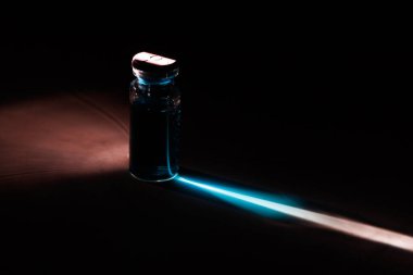 Beyaz mermer bir yüzeyde, rengini klinik laboratuvar için siyah bir arkaplanda yansıtan bir ışık demeti ile estetik ilaç şişesi..