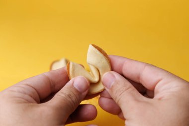 Dramatik gölgelerle dolu sarı bir arka planda insan eli çıtır bir fal kurabiyesi tutuyor. Gelecek, kader ve başarı için ideal..