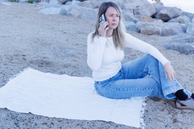 Genç çekici sarışın kadın deniz kenarında akıllı telefonunu kullanıyor. Yaz tatillerinde gençliği, özgürlüğü ve bağlılığı temsil etmek için mükemmel....