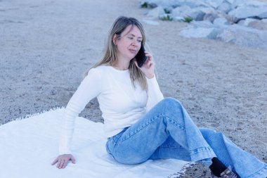 Sahilde akıllı telefonunu kullanan sarı saçlı çekici bir kız. 2026 'da yaz hayatını, iletişimi ve modayı temsil etmek için harika bir yöntem.!!