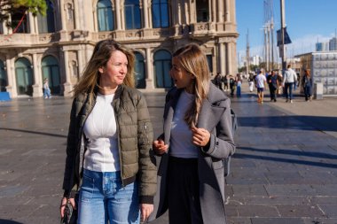 İskelede birlikte yürüyen neşeli kadınlar. Modern şehir manzarasında sakin bir gezinti yaparken sohbetlerine odaklanırlar....
