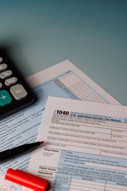 15 Nisan gelir vergisi konsepti renkli form 1040 ve araçlar. Hesap makinesi ve ofis malzemeleriyle dolu bir masanın üzerindeki pencereden güzel bir güneş ışığı..