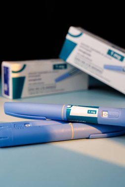 Modern GLP-1 semaglutid kalemler mavi yüzeyde kutuları var. Obezite tedavisi, insülin kontrolü ve tıbbi araştırma için mükemmel bir görsel..