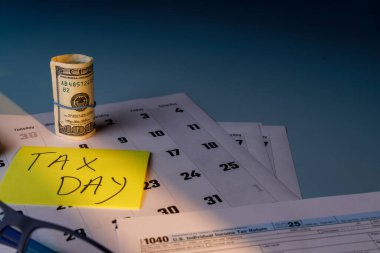 Üzerinde sarı not kağıdı ve IRS belgeleri olan modern ofis masası. Masada mavi gözlükler, iş aletleri ve vergi formlarıyla sıcak güneş ışığı.