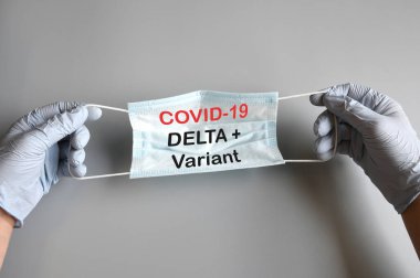 Mavi antiviral maskeli mavi eldivenli doktorun elleri ve Covid-19 Delta + Variant mesajı. COVID-19 Delta Varyant türü koruma kavramı.