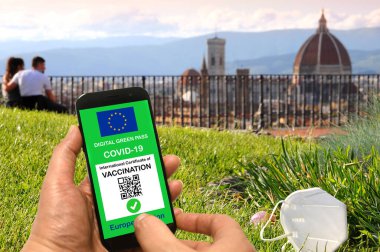 Avrupa Birliği 'nin dijital yeşil geçiş kartı ve ekranında QR kodu bulunan bir cep telefonu maskesi ve İtalya' nın Floransa Katedrali 'ne hayran turistler.