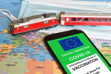 Avrupa Birliği 'nin akıllı telefondaki dijital yeşil geçiş kartı. Model tren ve coğrafi harita üzerinde cerrahi maskeler. Coronavirus sırasında Yeşil Geçişli Güvenli Seyahat Konsepti