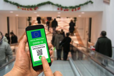 Alışveriş merkezinde elinde Covid-19 için Avrupa Birliği dijital yeşil kartı olan bir akıllı telefon tutan bir adam. Coronavirus ve Yeşil Geçit için güvenlik kavramı